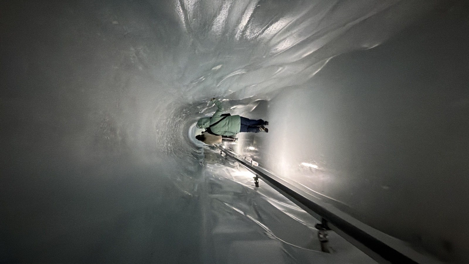 A lit tunnel carved through glacier ice, the walls polished smooth, curving away into the distance