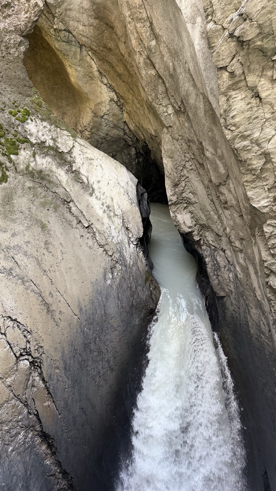 Grey glacial meltwater roaring through a narrow polished rock chasm deep inside a mountain