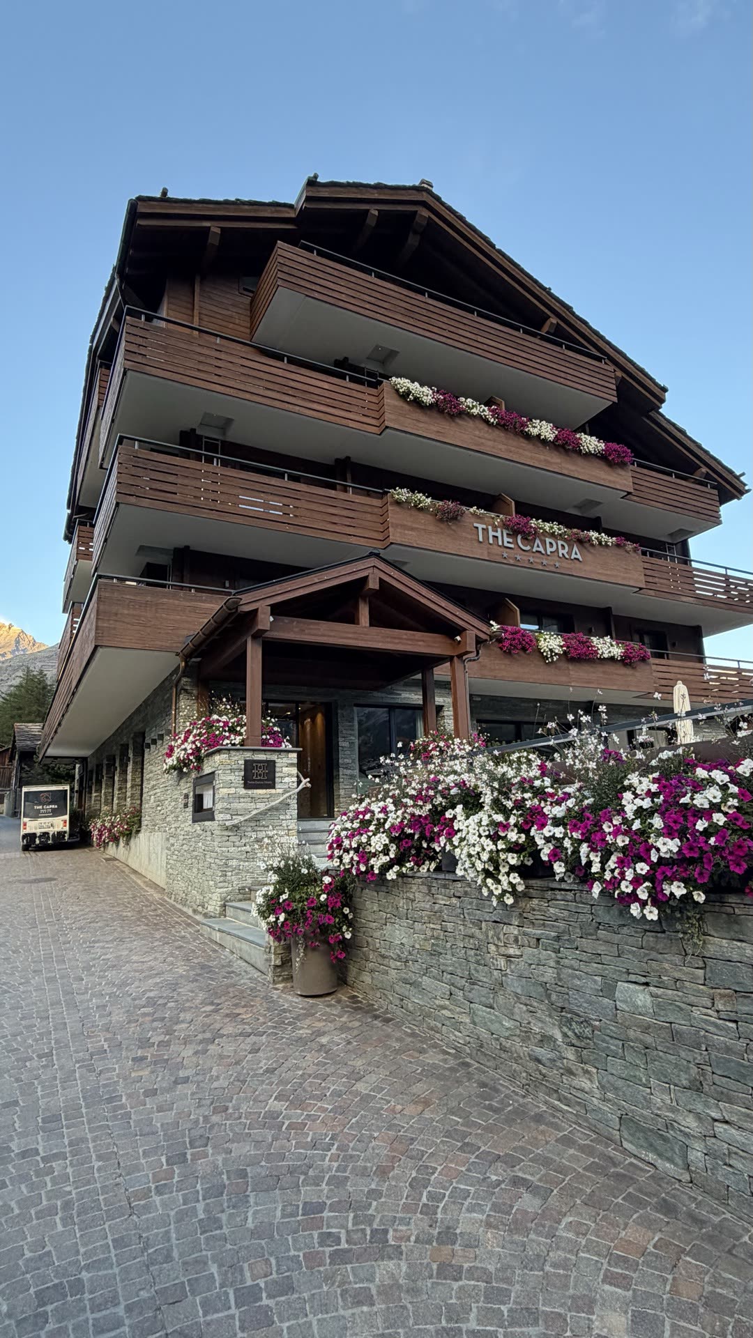 The timber and stone entrance of The Capra hotel with flower boxes along the balconies