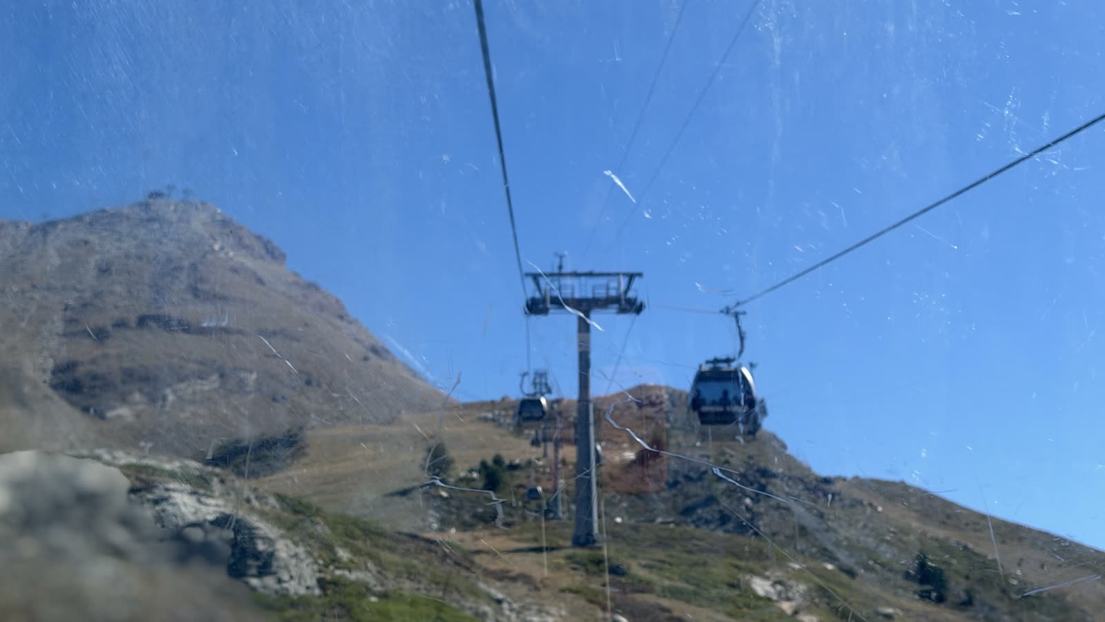 Gondola cabins on a cable rising over a bare mountainside under a blue sky