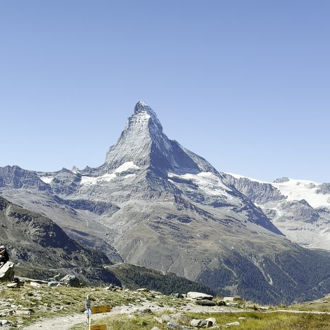 The Matterhorn against a clear sky, seen from a grassy trail with a signpost in the foreground