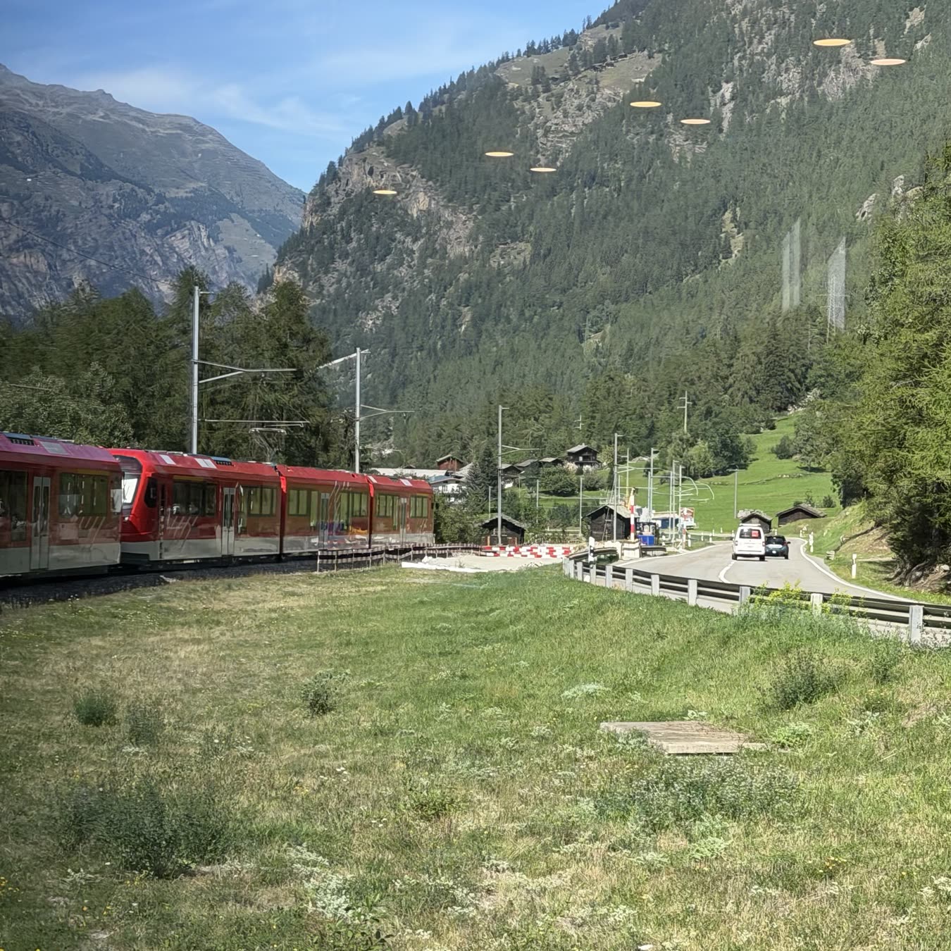 A red train at a small valley station with wooded slopes behind