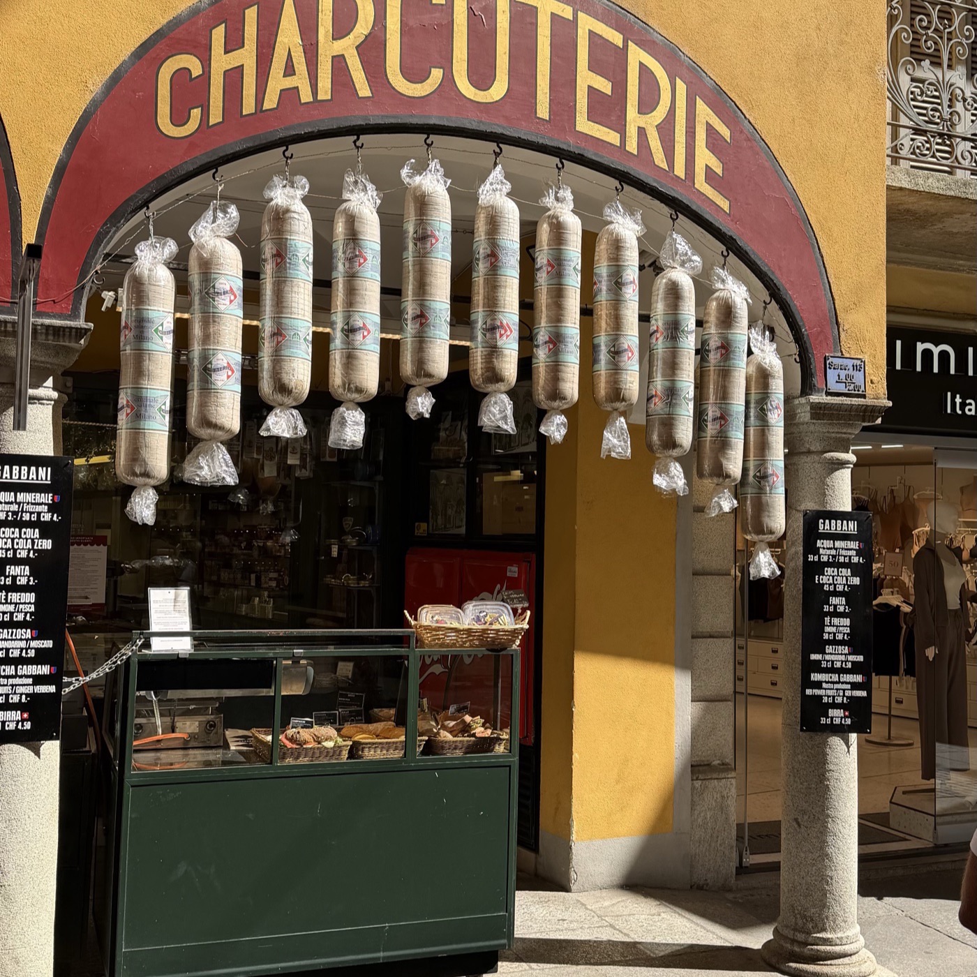 A charcuterie shop front with salami hanging under a red awning that reads Charcuterie