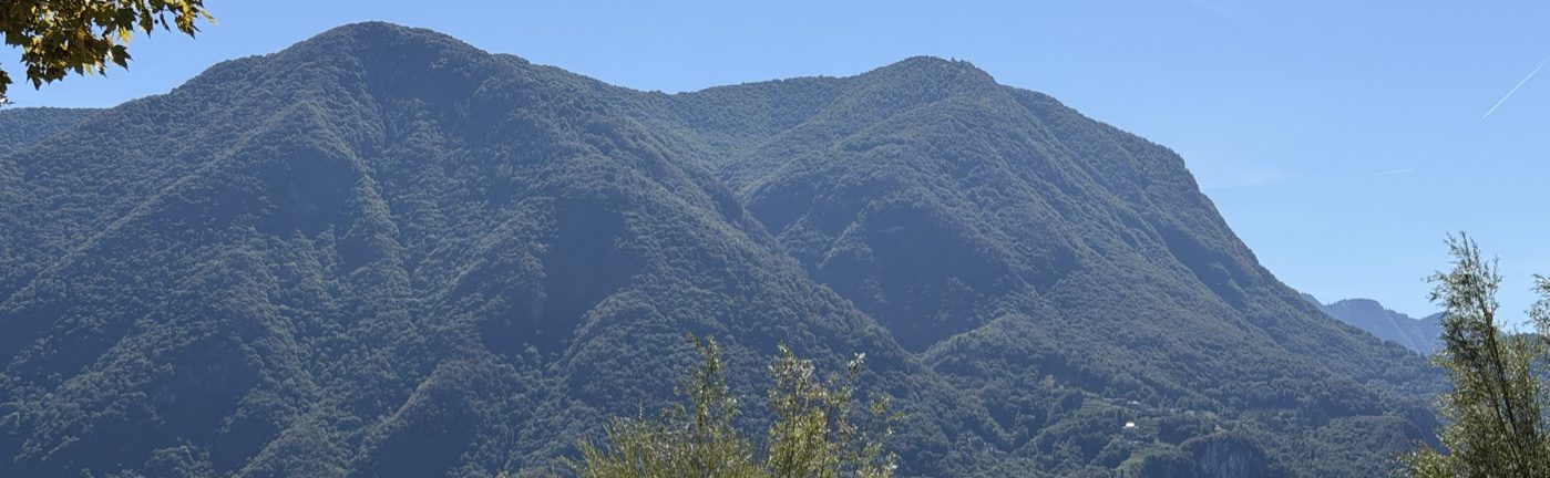 A wooded mountain ridge across Lake Lugano under a clear morning sky