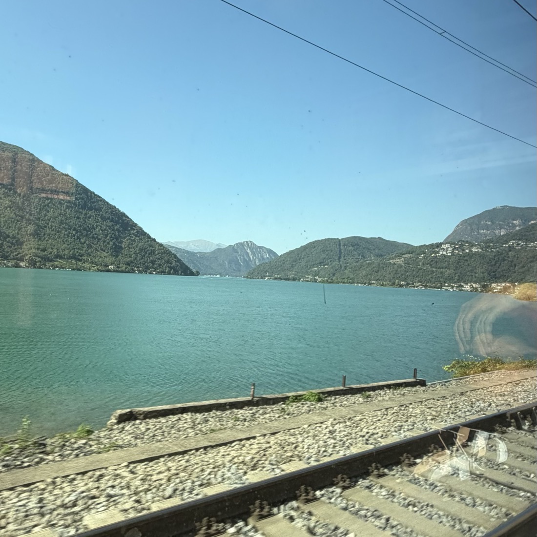 Railway track and a turquoise lake with green hills seen through a train window
