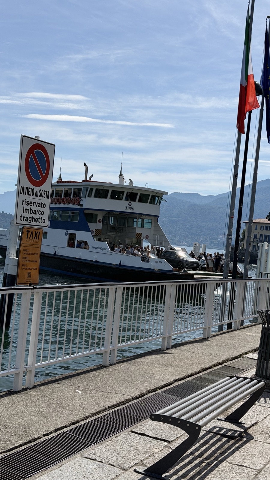 A white and blue car ferry docked at a lakeside pier beside a no-parking sign