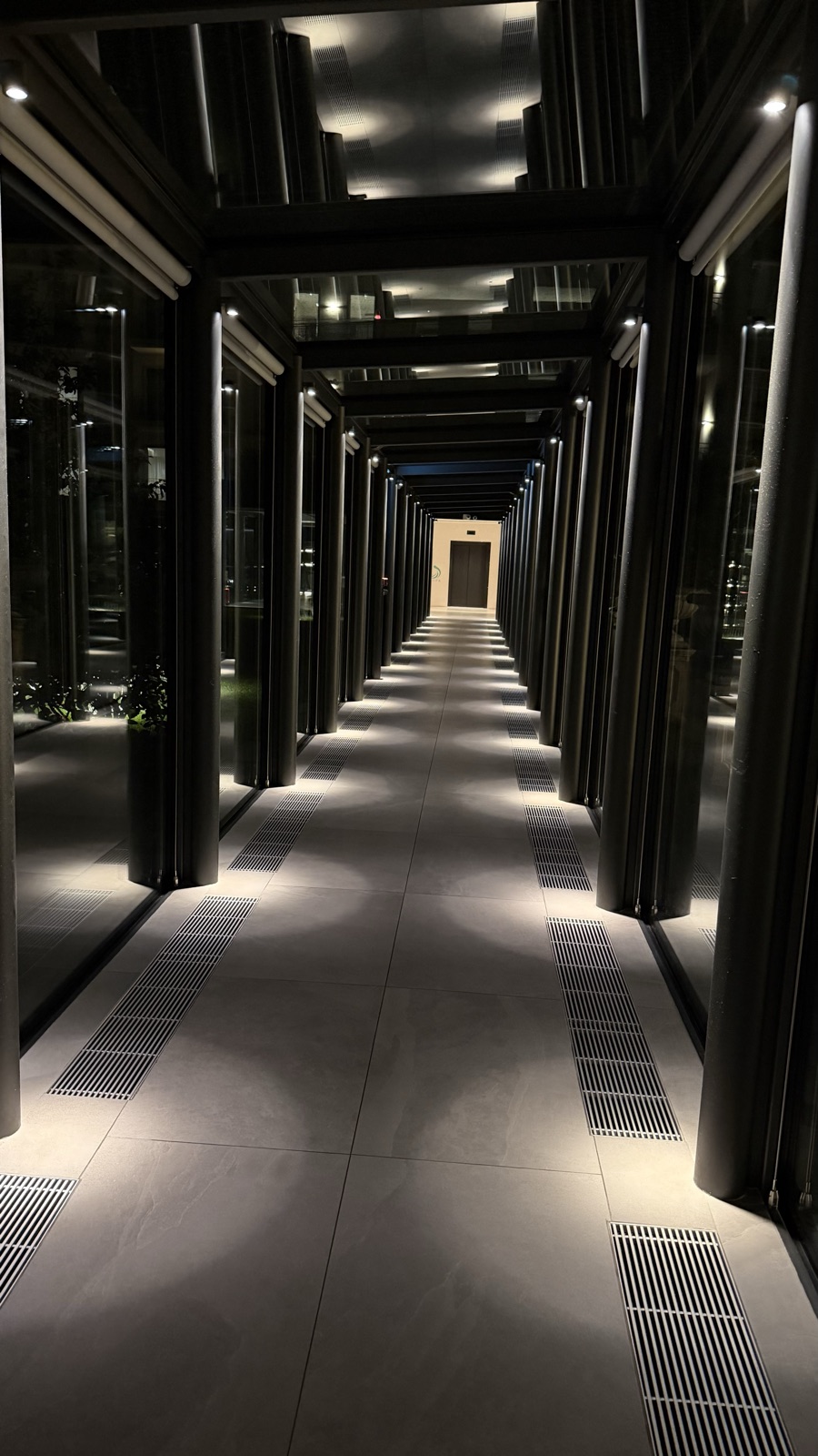 A long hotel corridor of dark mirrored columns lit from above, narrowing to a single door