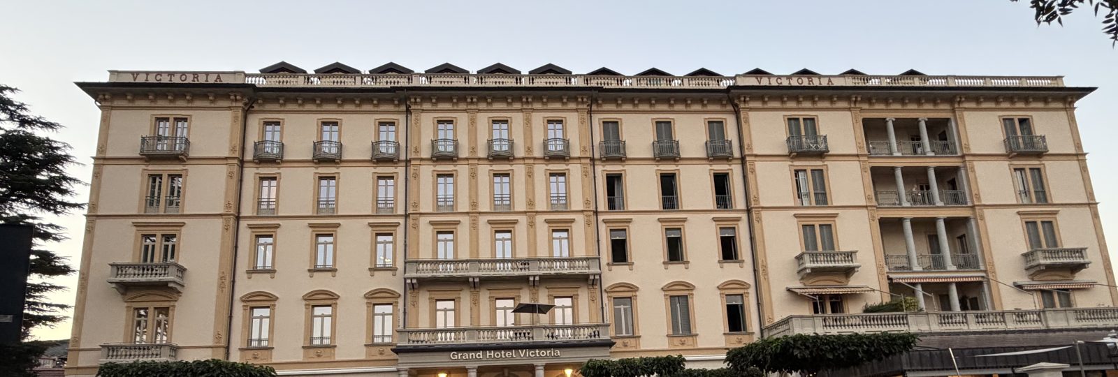 The upper floors of a grand cream hotel facade with shuttered windows and the name over the entrance, at dusk