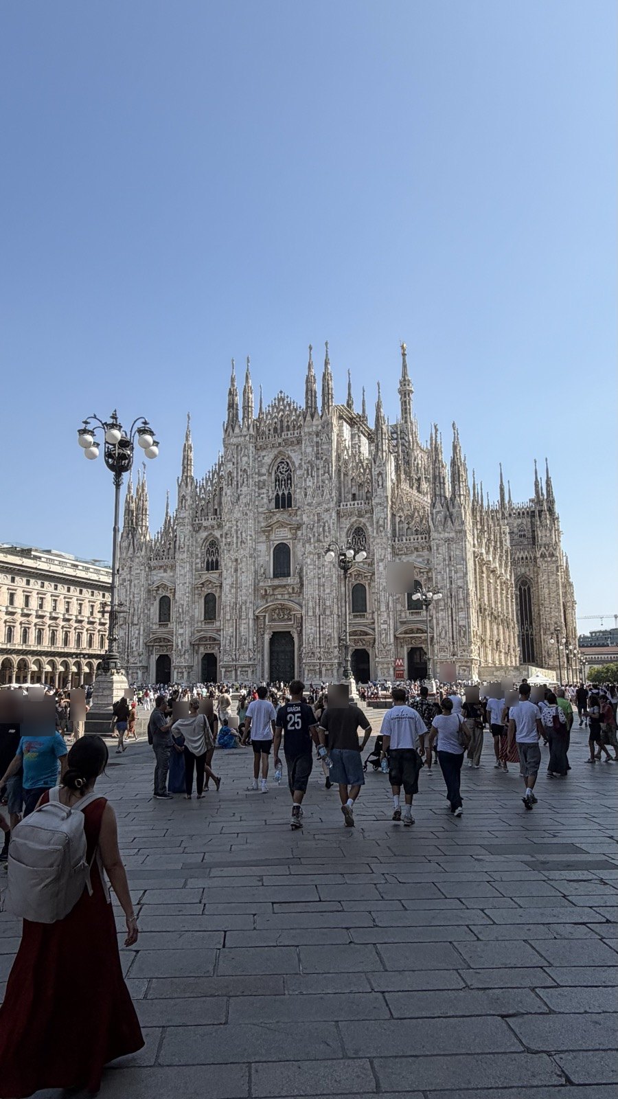 Milan Cathedral's white marble facade and spires under a clear blue sky, with visitors crossing the piazza