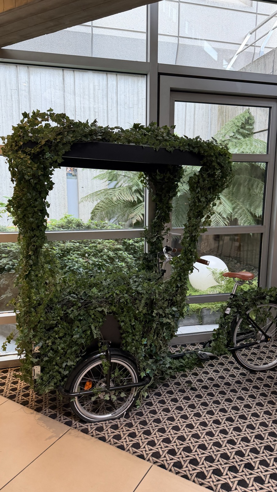 A hotel lobby with a patterned carpet and a cargo bike covered in climbing plants