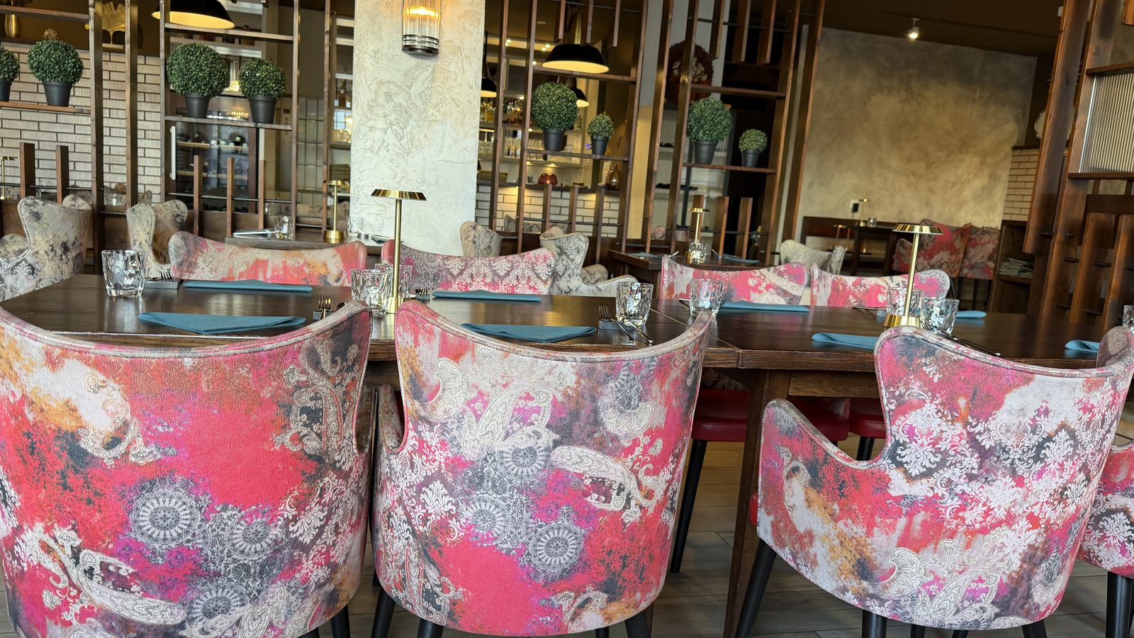 Inside Gourmindia in Lucerne: pink patterned armchairs, wood-slat walls and beaded pendant lamps, empty tables before the evening rush
