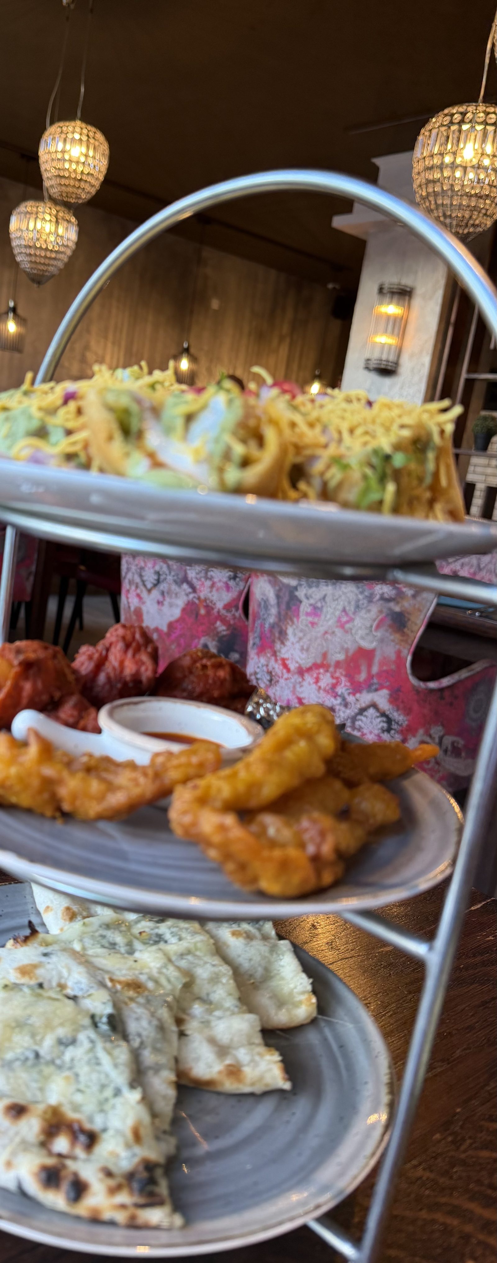 A three-tier stand at Gourmindia: cheese naan on the bottom plate, fried pakoras and tandoori pieces with a chutney in the middle, a chaat topped with sev on the top plate