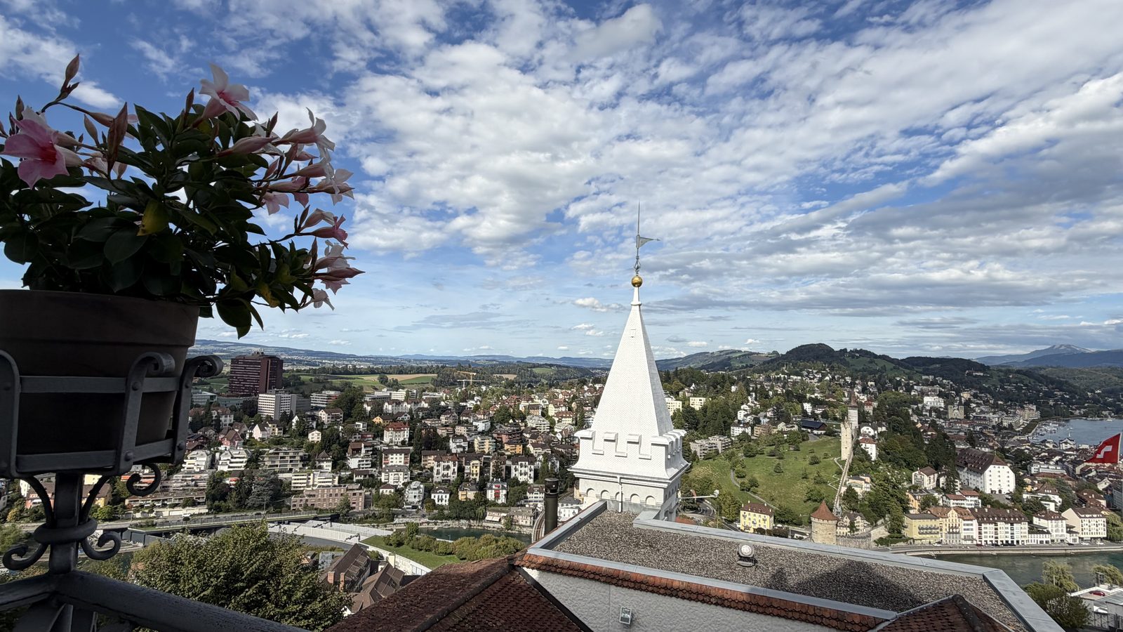 The view from the Château Gütsch terrace across the roofs to a church spire and the lake, with pink flowers in a planter on the railing