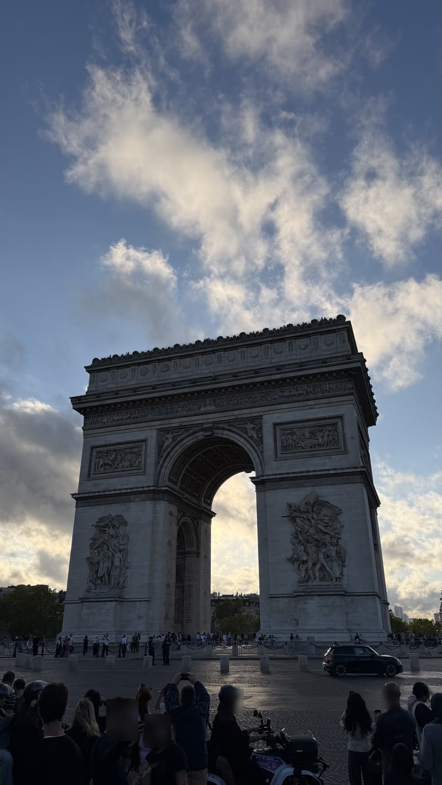 The Arc de Triomphe in late-afternoon light, seen from the ground with the sky behind it