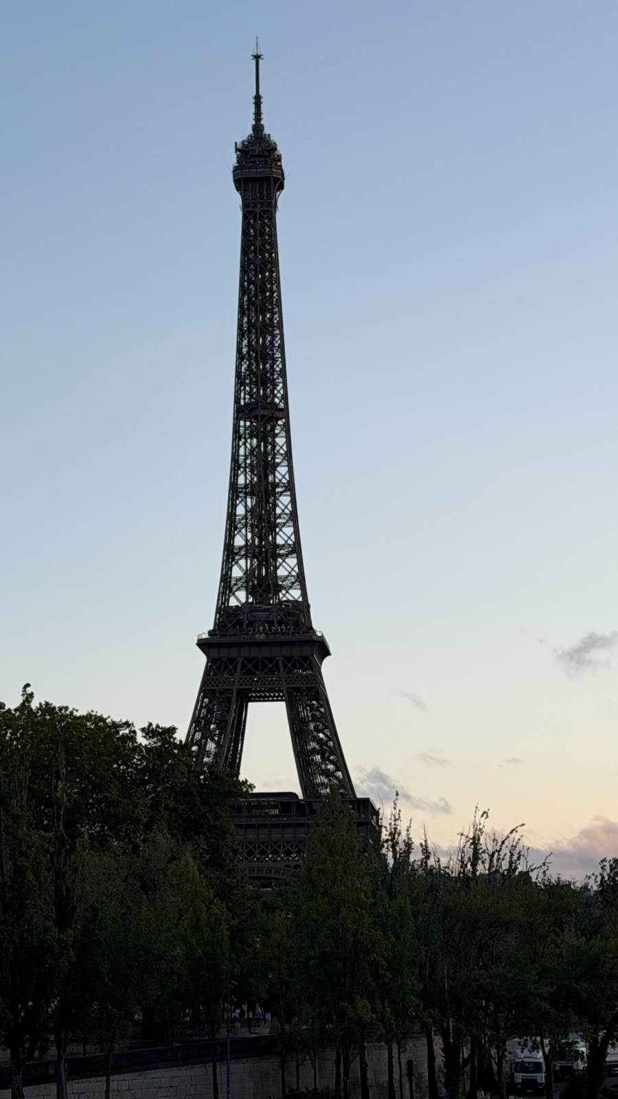 The Eiffel Tower at dusk from across the Seine, with river boats below and a pink and blue sky