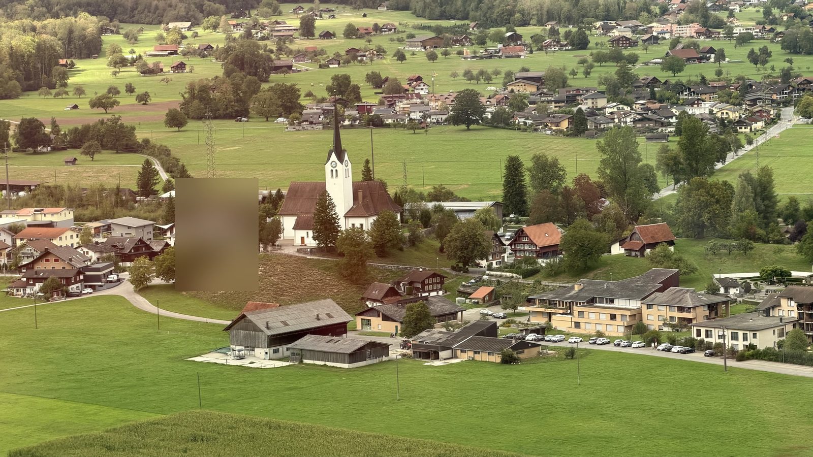 A green valley with a church spire and wooden farmhouses seen from a moving train near Giswil