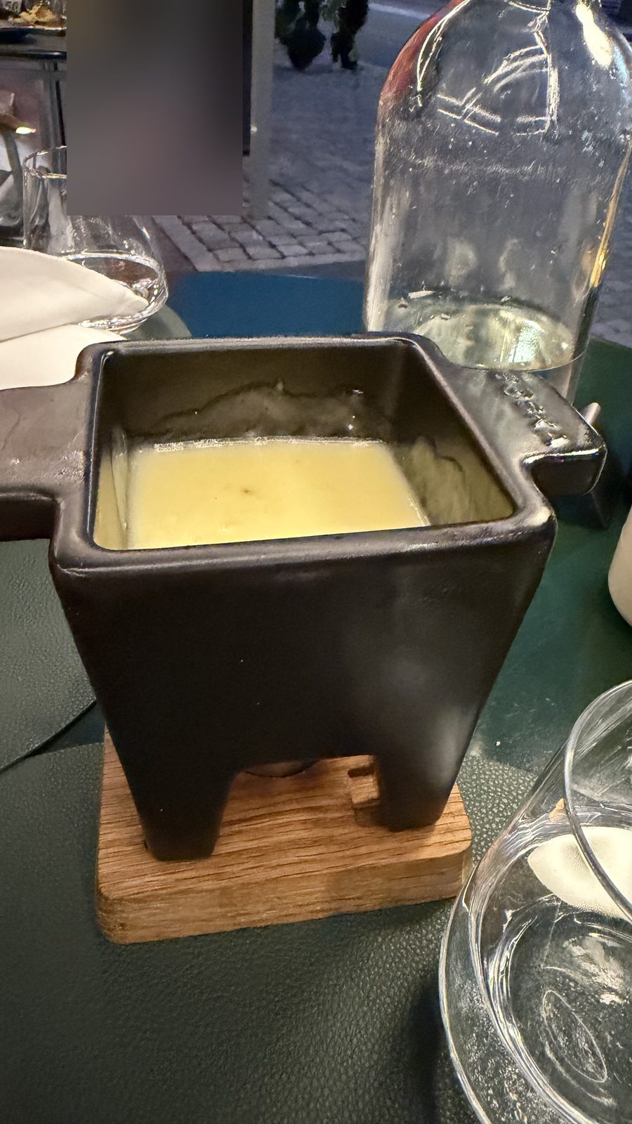 A cheese fondue pot on a wooden board on a restaurant table in the evening
