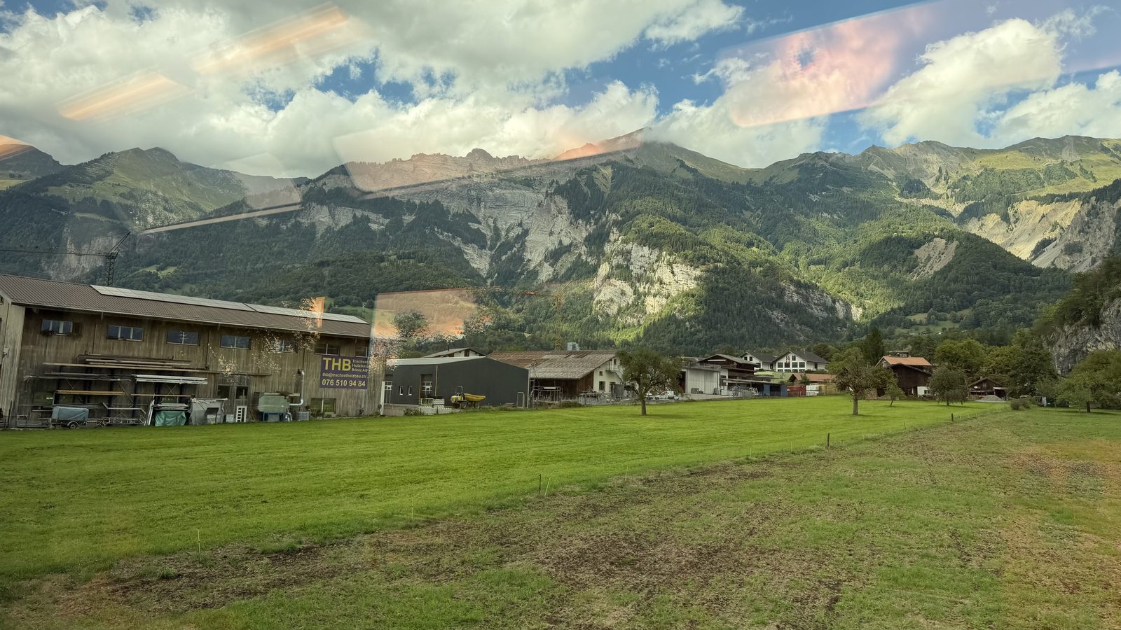 Turquoise water of Lake Brienz with a steep wooded mountain behind it seen from a train window